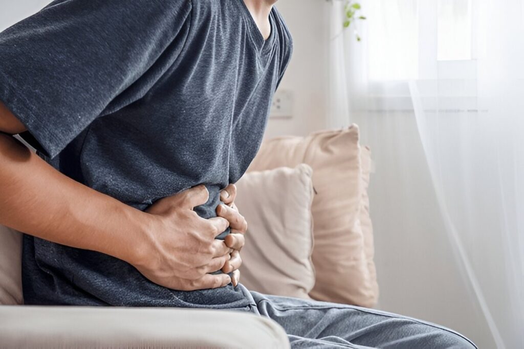 Man sitting down, clutching his stomach with both hands due to pain or discomfort.