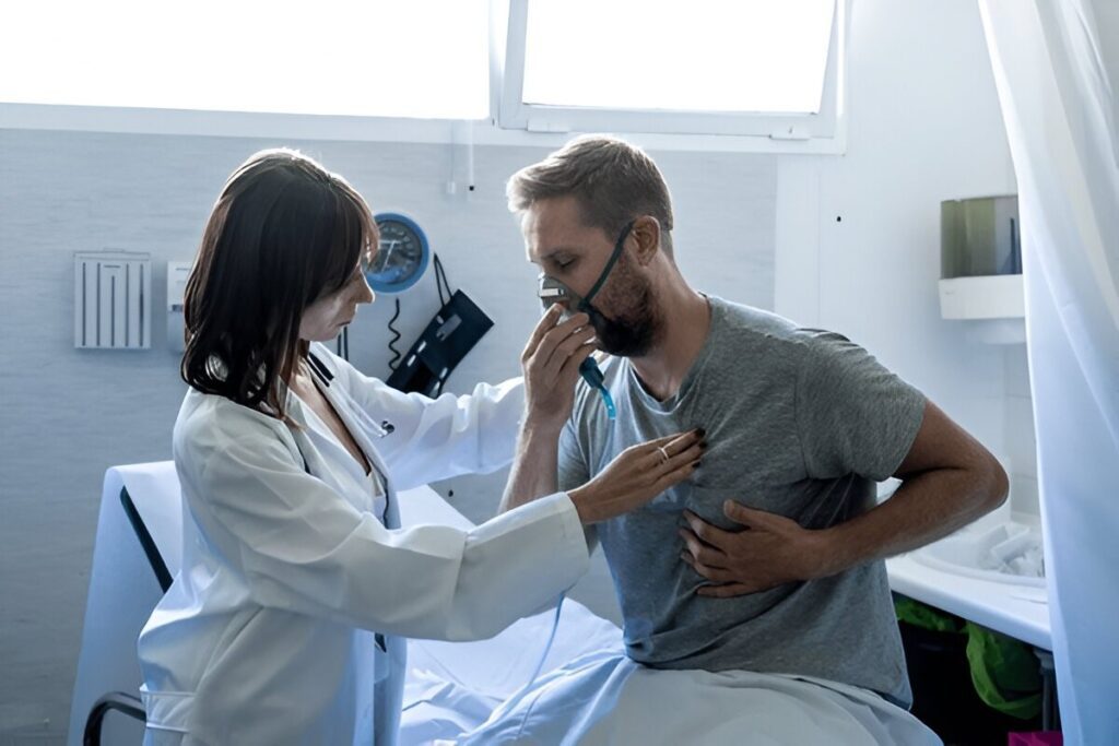 Doctor listening to a male patient's chest with a stethoscope while he wears an oxygen mask.