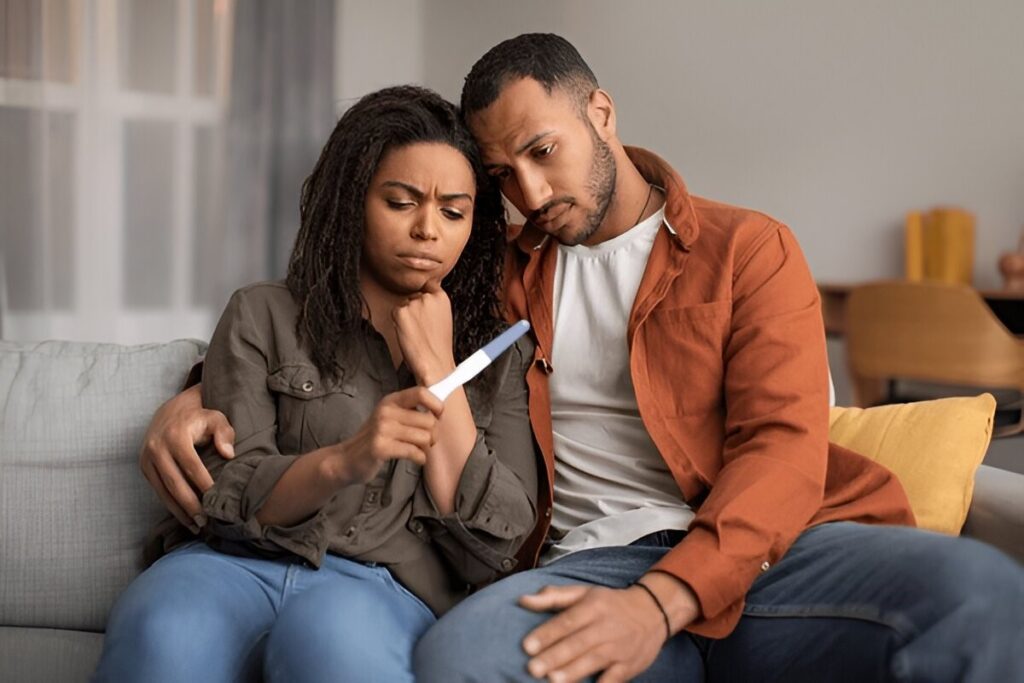 Disappointed or sad couple on a couch looking at a negative pregnancy test, suggesting a reproductive health issue or fertility struggles.